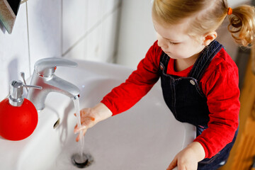 Cute little toddler girl washing hands with soap and water in bathroom. Adorable child learning...