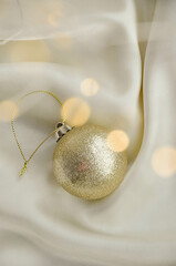 Gold Christmas Ornament on Soft White Fabric. Christmas decoration featuring a glittering golden bauble resting on a smooth white fabric background with soft, warm fairy lights, minimalism and winter-