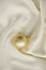 Gold Christmas Ornament on Soft White Fabric. Christmas decoration featuring a glittering golden bauble resting on a smooth white fabric background with soft, warm fairy lights, minimalism and winter-