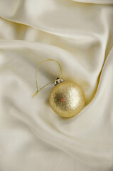 Gold Christmas Ornament on Soft White Fabric. Christmas decoration featuring a glittering golden bauble resting on a smooth white fabric background with soft, warm fairy lights, minimalism and winter-