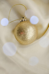 Gold Christmas Ornament on Soft White Fabric. Christmas decoration featuring a glittering golden bauble resting on a smooth white fabric background with soft, warm fairy lights, minimalism and winter-