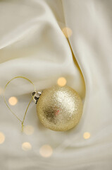 Gold Christmas Ornament on Soft White Fabric. Christmas decoration featuring a glittering golden bauble resting on a smooth white fabric background with soft, warm fairy lights, minimalism and winter-