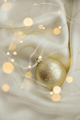 Gold Christmas Ornament on Soft White Fabric. Christmas decoration featuring a glittering golden bauble resting on a smooth white fabric background with soft, warm fairy lights, minimalism and winter-