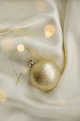 Gold Christmas Ornament on Soft White Fabric. Christmas decoration featuring a glittering golden bauble resting on a smooth white fabric background with soft, warm fairy lights, minimalism and winter-
