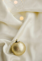 Gold Christmas Ornament on Soft White Fabric. Christmas decoration featuring a glittering golden bauble resting on a smooth white fabric background with soft, warm fairy lights, minimalism and winter-
