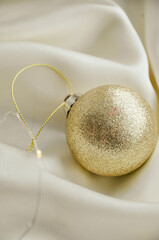 Gold Christmas Ornament on Soft White Fabric. Christmas decoration featuring a glittering golden bauble resting on a smooth white fabric background with soft, warm fairy lights, minimalism and winter-