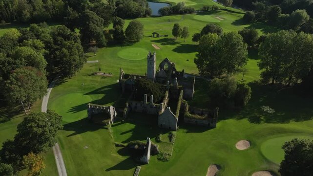 Franciscan Friary, Adare, County Limerick, Ireland, September 2024. Drone orbits counter clockwise above the ruins in middle of golf course on a bright sunny day with Adare Manor in the distance.
