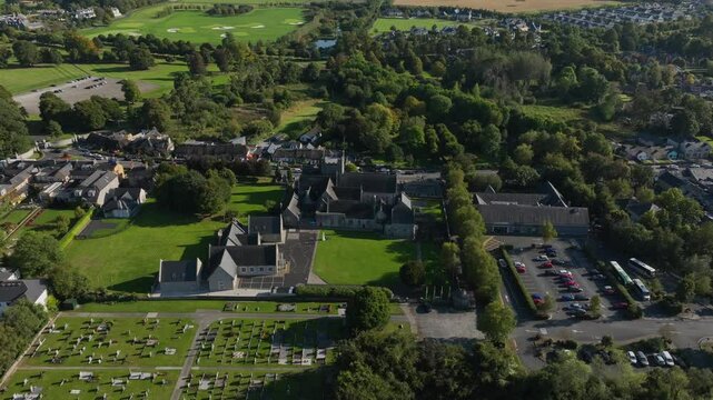 Holy Trinity Abbey Church, Adare, County Limerick, Ireland, September 2024. Drone orbits clockwise above cemetery to showcase church buildings and scenic traditional homes on the River Maigue.