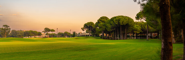 A panoramic golf course framed by tall trees and bathed in the warm glow of twilight, offering a serene and relaxing environment.
