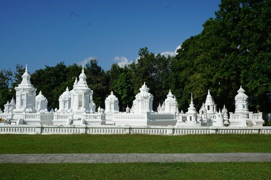 A row of white chedis, or Buddhist stupas, northern thailand, set against a backdrop of lush green trees and a clear blue sky.