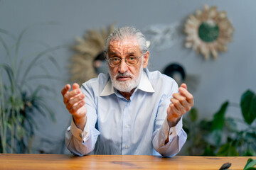 close-up of a very elderly gray-haired grandfather in a blue shirt with a slight smile, sitting...