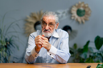 close-up of a very elderly gray-haired grandfather in a blue shirt with a slight smile, sitting...