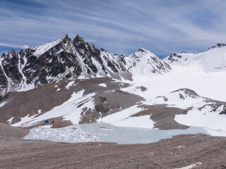 Frozen ice-covered lake in the mountains in winter. Drone view of snow-capped peaks and mountain range. Beautiful clouds on the blue sky. Vivid photographs of natural landscapes of the Tien Shan.