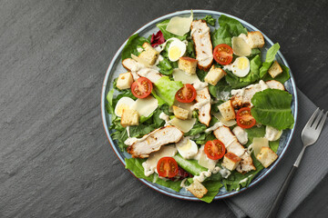 Tasty Caesar salad with chicken and tomatoes served on dark gray textured table, flat lay. Space for text