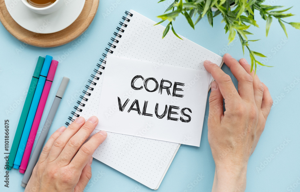 Aufkleber notebook with text inside core values on table with coffee, laptop and some sheet of papers with cha