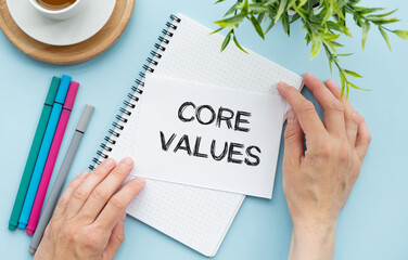Notebook with text inside Core Values on table with coffee, laptop and some sheet of papers with...