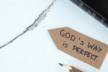 God's way is perfect, handwritten quote on paper arrow with holy bible book on white marble...