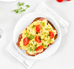 Scrambled eggs with microgreen, bacon and tomatoes on bread