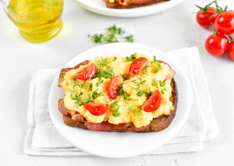 Scrambled eggs with microgreen, bacon and tomato slices on bread