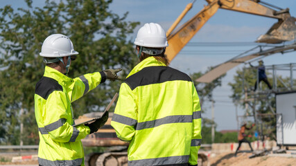 Caucasian white civil engineer, architect, or construction worker is wearing a safety suit while inspecting building construction on site and verifying blueprints or drawing plans.