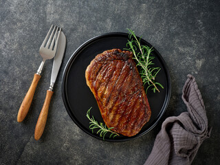 Beef Steak medium rare on black plate, surfed with tableware on black stone table with ample copy space. Dark background. Top view. Copy space.