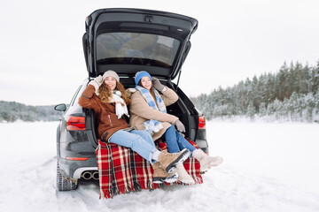 Two young women near a car on a snowy road.  Traveling in Winter.