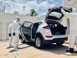 Hygiene personnel disinfecting a grey vehicle from viruses and bacteria with biological equipment
