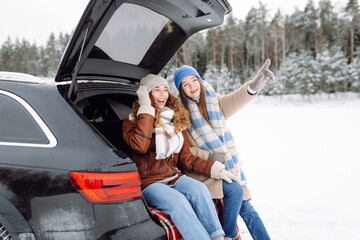 Two young women near a car on a snowy road.  Traveling in Winter.