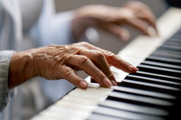 hands close up an elderly woman sits at the piano playing a melody learning new chords old age...