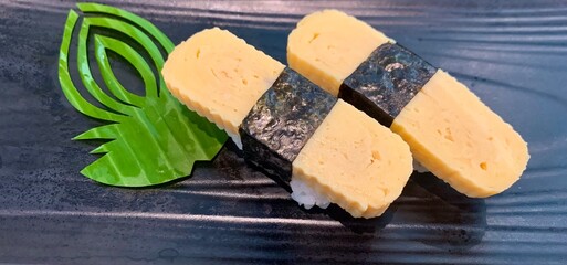 Tamako egg sushi in black plate background, featuring perfectly folded layers of sweet egg atop rice Serve in black plate
