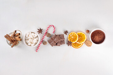 Ingredients for making hot chocolate, traditional winter cocoa tasty drink. Chocolate pieces, cocoa powder, milk, marshmallows, spices, cinnamon, nuts, dried orange, top view copy space