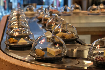 Cheese slices under a transparent cover, on a conveyor belt.