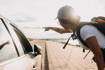 Asian woman traveller carrying yellow backpack, asking a drive while traveling, asking the way, walking on foot path at countryside, solo travel concept.