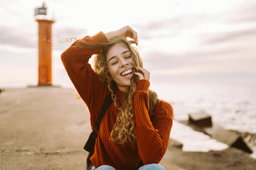 Portrait of woman enjoying a breezy day near a vibrant red lighthouse at sunset. Travel, weekend,...