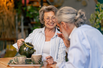 home happy old age elderly couple pleasant memories leisure in old age wife brings tea for her husband sitting at the table care in old age pours tea into cups