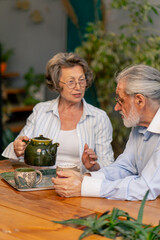 home happy old age elderly couple pleasant memories leisure in old age wife brings tea for her husband sitting at the table care in old age pours tea into cups