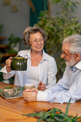 home happy old age elderly couple pleasant memories leisure in old age wife brings tea for her husband sitting at the table care in old age pours tea into cups