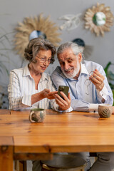 elderly people sitting at a table together watching social networks on the phone funny videos happy old age elderly couple pleasant memories leisure time in old age warm feelings support in old age