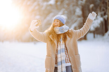 Happy Woman traveling during the Christmas season takes a selfie video in winter forest against snow-covered trees and falling snow.