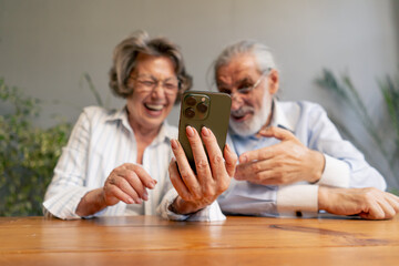 elderly people sitting at a table together watching social networks on the phone funny videos happy old age elderly couple pleasant memories leisure time in old age warm feelings support in old age