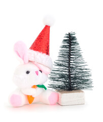 A toy bunny in a Santa Claus hat near a New Year's tree.