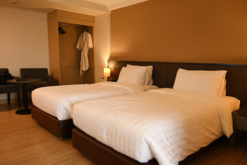 A cozy hotel room with two neatly arranged twin beds, soft lighting, a wardrobe with robes, and a sitting area, creating a perfect space for relaxation