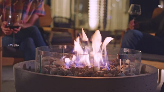Shot of a fire pit with two people drinking wine in the background