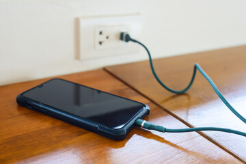 A smartphone while charging on the wooden table in the coffee shop,  by connecting directily to the...