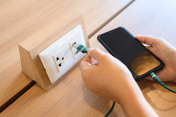 Closeup a woman is plugging her phone charger into a USB socket built into the desk