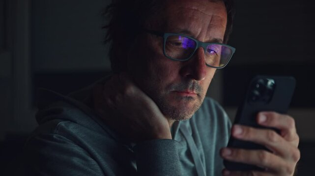 Bored man using smartphone late at night, browsing the internet or using social media apps, 4K