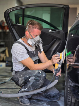A skilled auto painter meticulously polishing a car to prepare it for painting, showcasing precision and craftsmanship in the workshop.