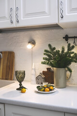 Imagine a charming setup with twinkling lights, on pine branches, mandarins on white plate, glasse of champagne on table of kitchen.