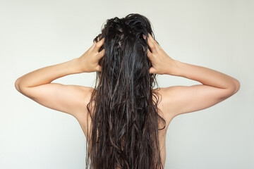 A young Caucasian brunette woman touching her beautiful long wet hair with her hands after shampooing. Back view