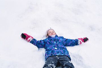 Happy and cheerful child lies on the snow outside in winter. Hello winter. Copy space